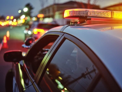Police car with flashing red and blue lights at a nighttime roadside scene with blurred traffic in the background.